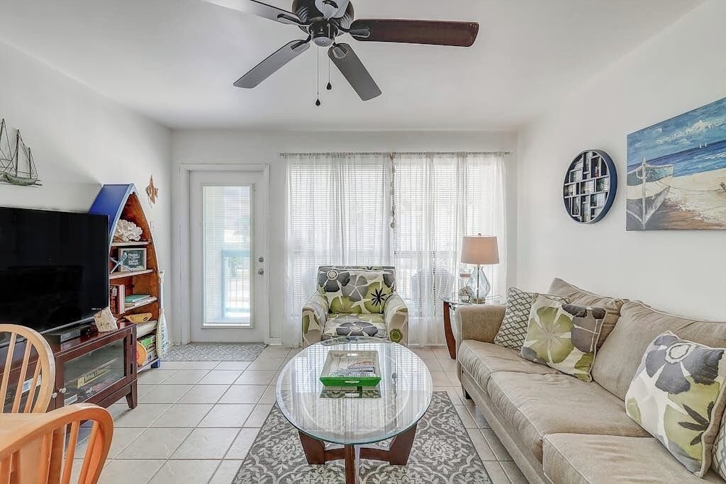 A living room with a television, a sofa, a coffee table, and a ceiling fan.