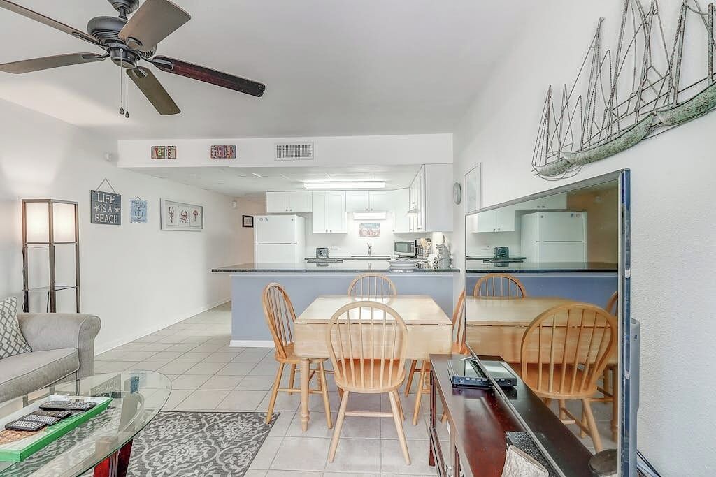 A modern kitchen with white cabinets, a dining area with wooden chairs, and a ceiling fan.