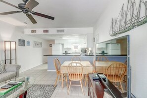 A modern kitchen with white cabinets, a dining area with wooden chairs, and a ceiling fan. - Nelray Shores at Seamist Condominiums (Port Aransas)