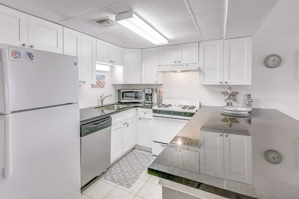 A modern kitchen with white cabinets, a refrigerator, a microwave, a stove, and a sink.