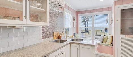 A kitchen with white cabinets, a granite countertop, a dishwasher, and a window with blinds.