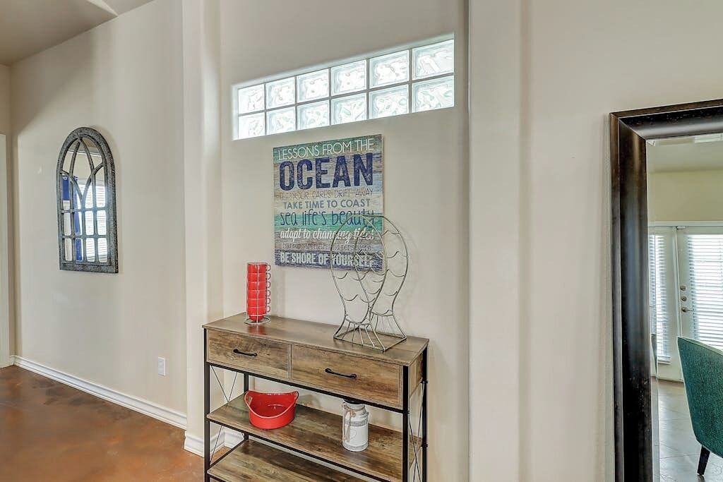 A hallway with a wooden cabinet, a framed quote on the wall, and a window with blinds.