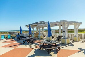 Un patio frente a la playa con mesas de picnic y sombrillas, con vista al océano.