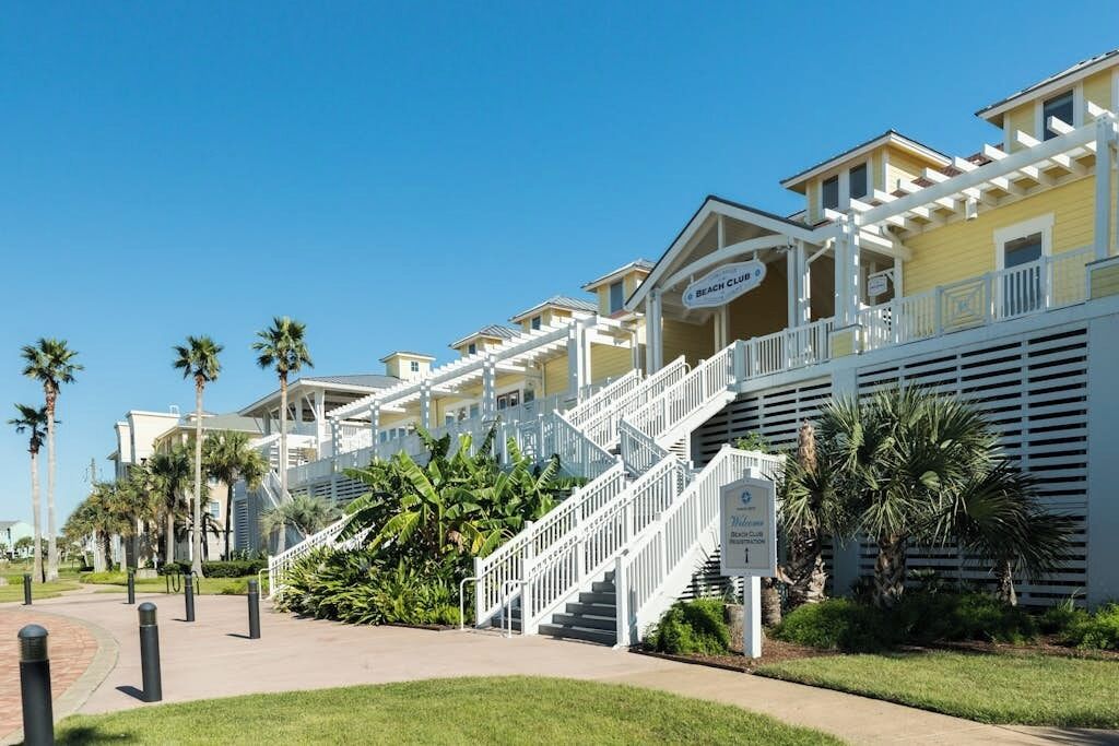 A beachfront hotel with multiple balconies, a central staircase, and palm trees.