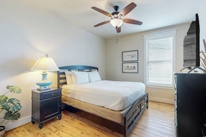 A bedroom with a bed, a nightstand, a ceiling fan, a window with blinds, and a plant. - Pointe West Resort - Beach Retreat (Galveston)