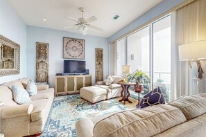 A spacious living room with a large window, a ceiling fan, and a flat-screen TV. - Diamond Beach Resort Seawall Stunner (Galveston)
