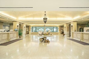 A spacious lobby with a central chandelier, a reception desk, and a large window providing a view of the outside. - Diamond Beach Resort Seawall Stunner (Galveston)