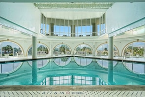 A large indoor swimming pool with a 3ft 6in depth, surrounded by multiple levels of seating and large windows. - Diamond Beach Resort Seawall Stunner (Galveston)