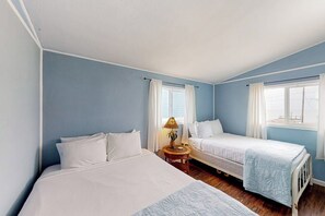 Ein Schlafzimmer mit zwei Betten, einem kleinen Tisch mit Lampe und einem Fenster mit Vorhängen.