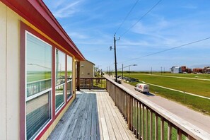 Eine Holzterrasse mit großen Fenstern mit Blick auf eine Straße und eine Rasenfläche.