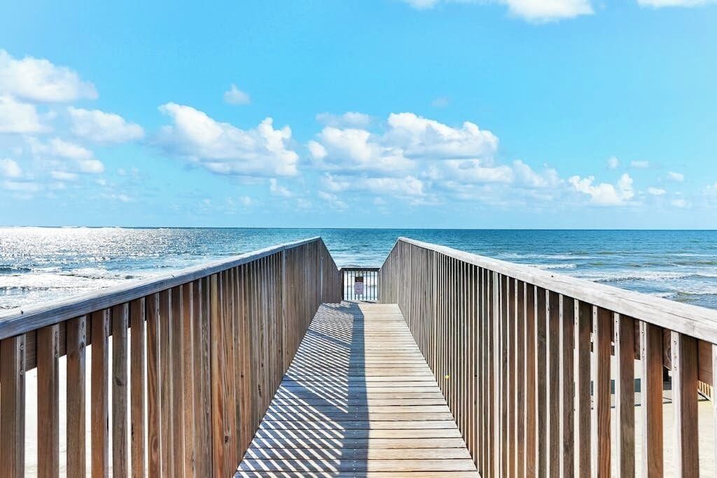 A wooden boardwalk leading to the ocean with a clear sky above.