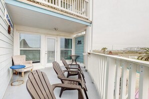 A balcony with a row of wooden chairs and a small round table, a white railing, and a view of the beach and distant buildings. - Seascape Condos #2121 (Galveston)
