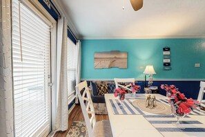 A dining area with a table, chairs, and a bench. There is a wall with a painting and a sign with words. - Seascape Condos #2121 (Galveston)