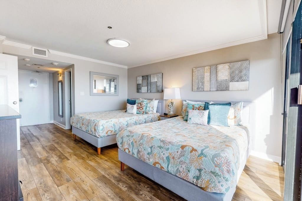 A bedroom with two beds, a bedside table, a lamp, and artwork on the wall.