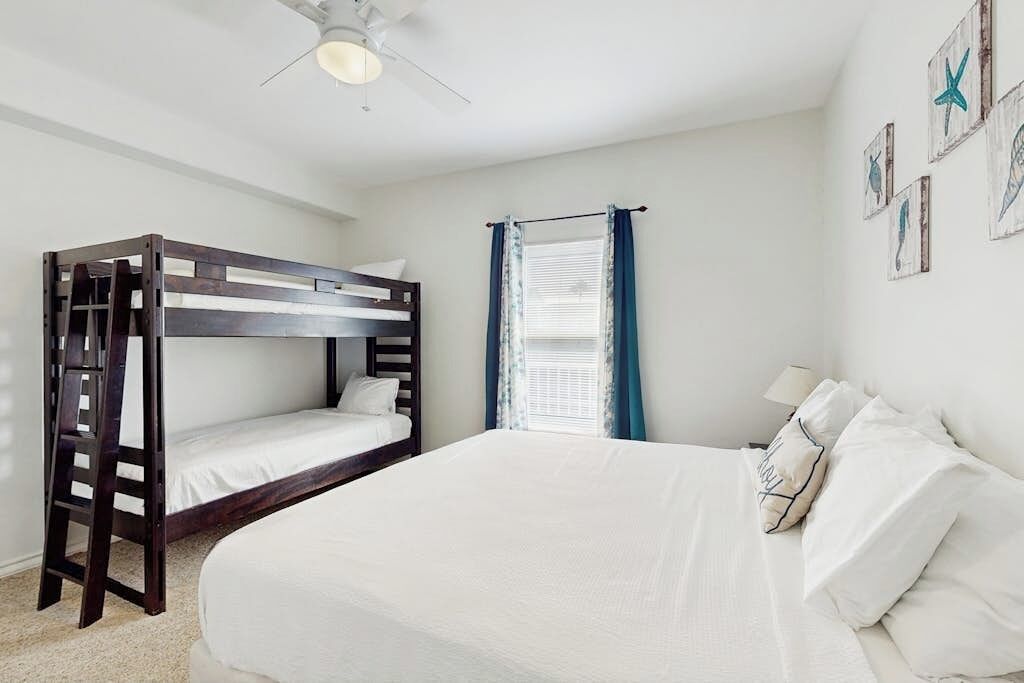 A bunk bed room with a ceiling fan, a window with curtains, and wall art.