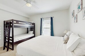 A bunk bed room with a ceiling fan, a window with curtains, and wall art. - Compass Condominiums B8 (Corpus Christi)