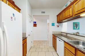 A kitchen with wooden cabinets, a white refrigerator, a granite countertop, and a stainless steel sink. - Compass Condominiums B8 (Corpus Christi)