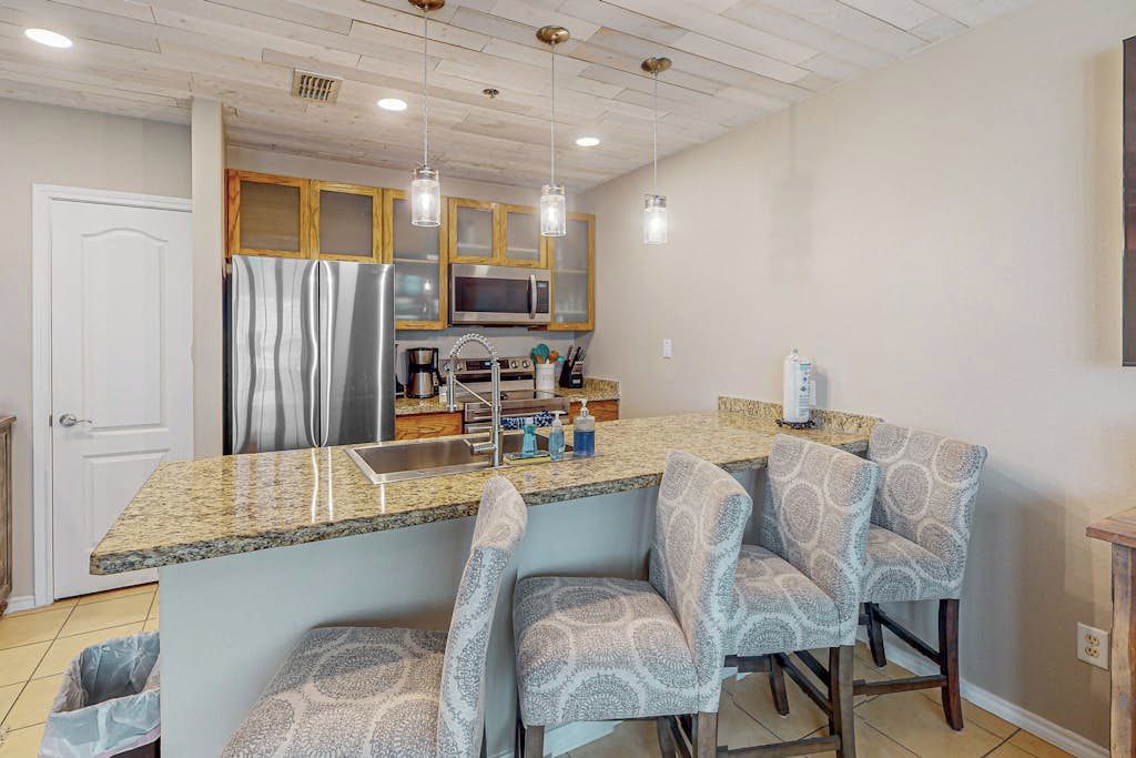 A kitchen with a granite countertop, stainless steel appliances, and a bar area with patterned chairs.