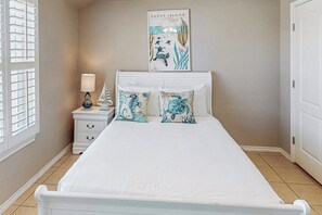 A bedroom with a bed, a nightstand, a lamp, and a wall-mounted poster. - Star Beachside Condominiums 106 (South Padre Island)