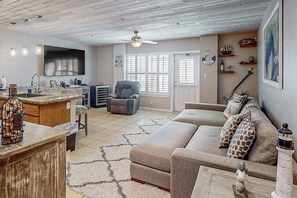 A spacious living room with a large sofa, a dining area with a kitchen counter, and a ceiling fan. - Star Beachside Condominiums 106 (South Padre Island)