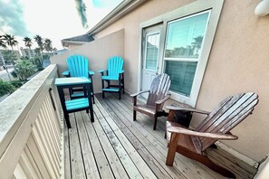 A wooden deck with four Adirondack chairs, a small table, and a window. - Star Beachside Condominiums 106 (South Padre Island)