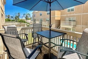 A balcony with a table and chairs, overlooking a swimming pool and buildings. - Star Beachside Condominiums 106 (South Padre Island)