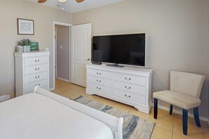 A bedroom with a bed, a TV, a dresser, a chair, and a door. - Star Beachside Condominiums 106 (South Padre Island)