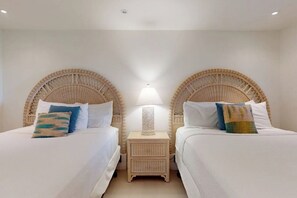 A room with two beds, each with a wicker headboard, a bedside table with a lamp, and a wall-mounted light. - Solare Garden Villa 220 (South Padre Island)