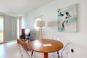 A modern dining area with a round table, chairs, a television, and artwork on the wall. - Solare Garden Villa 220 (South Padre Island)