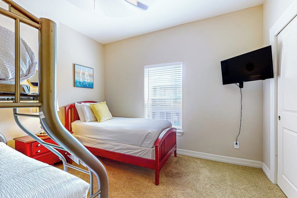 A bedroom with a bunk bed, a single bed, a television mounted on the wall, and a window with blinds.