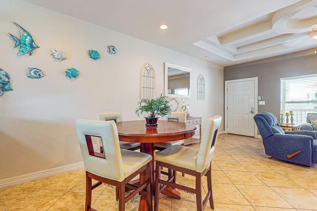 A dining area with a round table and chairs, a potted plant, decorative fish wall art, a mirror, and a door in the background.