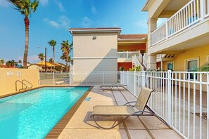 Ein Swimmingpool mit Liegestühlen und einem weißen Zaun, umgeben von Palmen und einem Gebäude mit Balkonen.