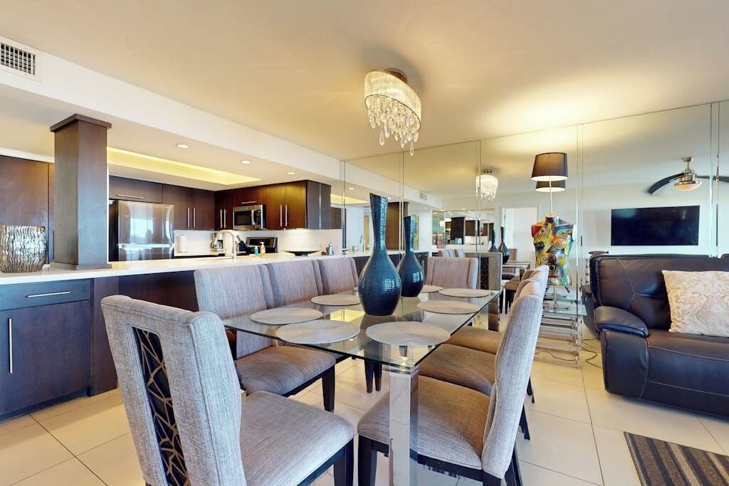 A modern kitchen with dark cabinetry, a central island, and a dining area with a glass table and chairs.