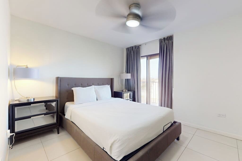 A hotel room with a bed, bedside tables, a ceiling fan, and a window with curtains.