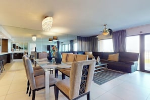 Ein modernes Wohnzimmer mit Essbereich, großen Fenstern und einer Chandelüster.
