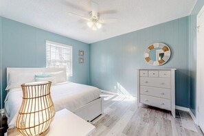 A bedroom with a bed, dresser, bedside lamp, and a ceiling fan. - Lazy Seagull Beach House - Upstairs (South Padre Island)