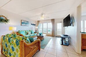 A living room with a sofa, a coffee table, a television, and a balcony door. - Saida Towers I #402 - Oceanfront, Pools & Hot Tub (South Padre Island)