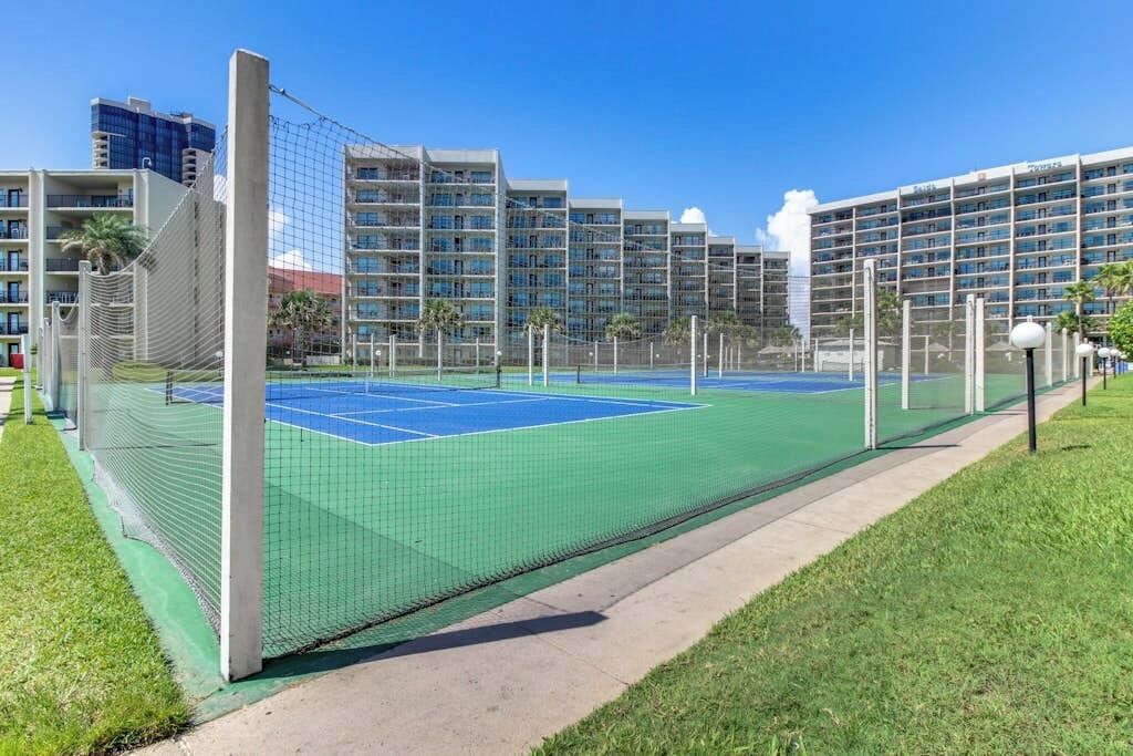 A tennis court with a net, surrounded by a fence, and adjacent to a building with multiple balconies.