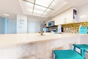 A kitchen with a white countertop, a microwave, and a sign indicating WiFi availability. - Saida Towers I #402 - Oceanfront, Pools & Hot Tub (South Padre Island)