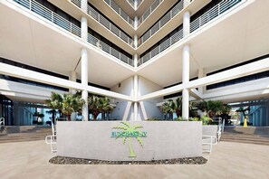 A modern atrium with a central column, palm trees, and a sign reading 'SUNCHASE IV'. - Sunchase IV #509 - Gulf & Bay Views, Pools & Gym (South Padre Island)