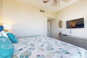 Ein Schlafzimmer mit einem Bett, einem Schminktisch, einem Fernseher und einem Spiegel an der Wand.