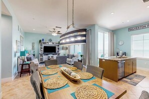 A modern living room with a dining area, kitchen, and a ceiling fan. - Diamond Beach Resort - A Shore Thing (Galveston)