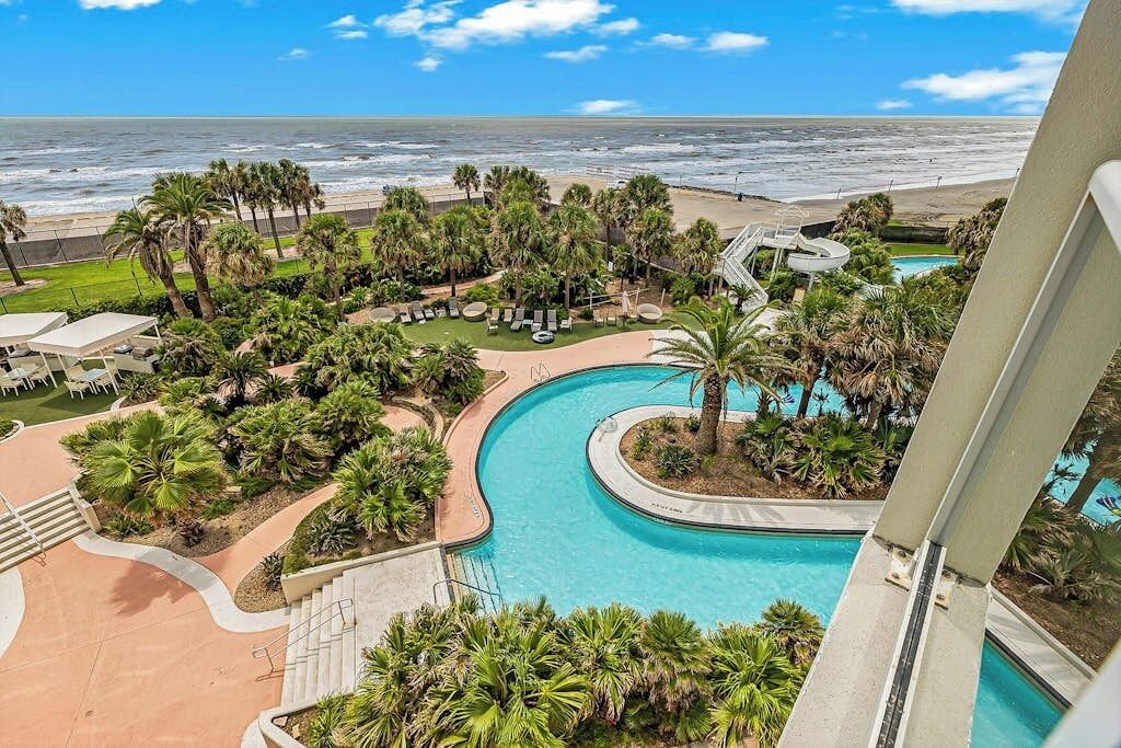 A resort with a pool, palm trees, and a view of the ocean.