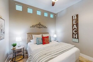 A bedroom with a bed, bedside tables, a decorative wall piece, and a ceiling fan. - Diamond Beach Resort - A Shore Thing (Galveston)