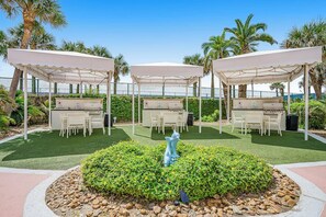 Three outdoor barbecue areas with tables and chairs, surrounded by greenery and palm trees. - Diamond Beach Resort - A Shore Thing (Galveston)