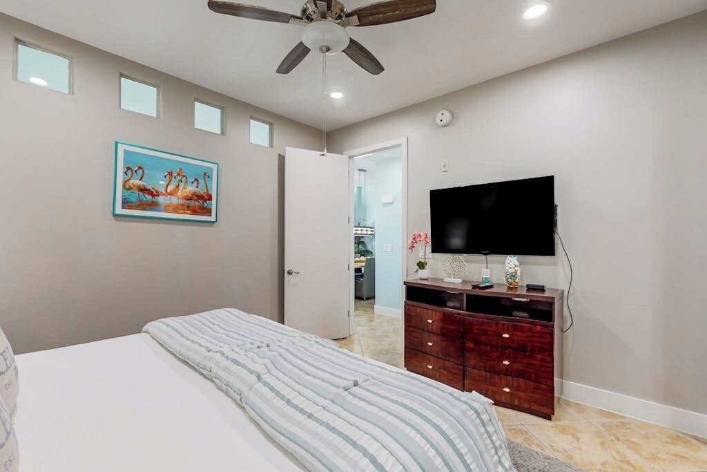 A bedroom with a bed, a ceiling fan, a TV, and a dresser.