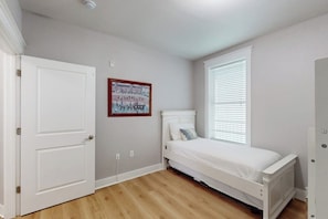 A bedroom with a single bed, a window with blinds, a door, and a wall-mounted picture. - Pointe West Resort - Sand Swept (Galveston)