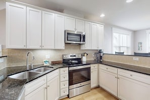 A modern kitchen with white cabinetry, a stainless steel oven, a microwave, and a granite countertop. - Pointe West Resort - Sand Swept (Galveston)