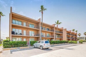 Un hotel de varios pisos con balcones, estacionamiento y palmeras.
