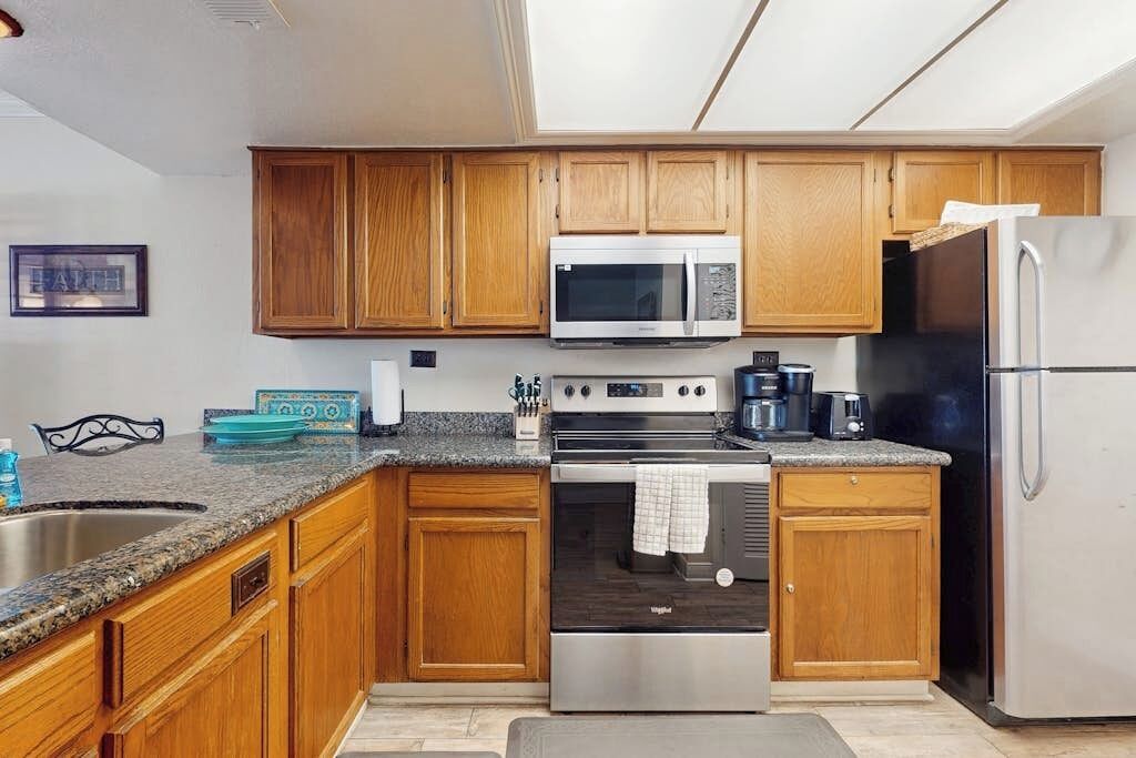 A kitchen with wooden cabinets, a stainless steel refrigerator, a microwave, a stove, and a sink.
